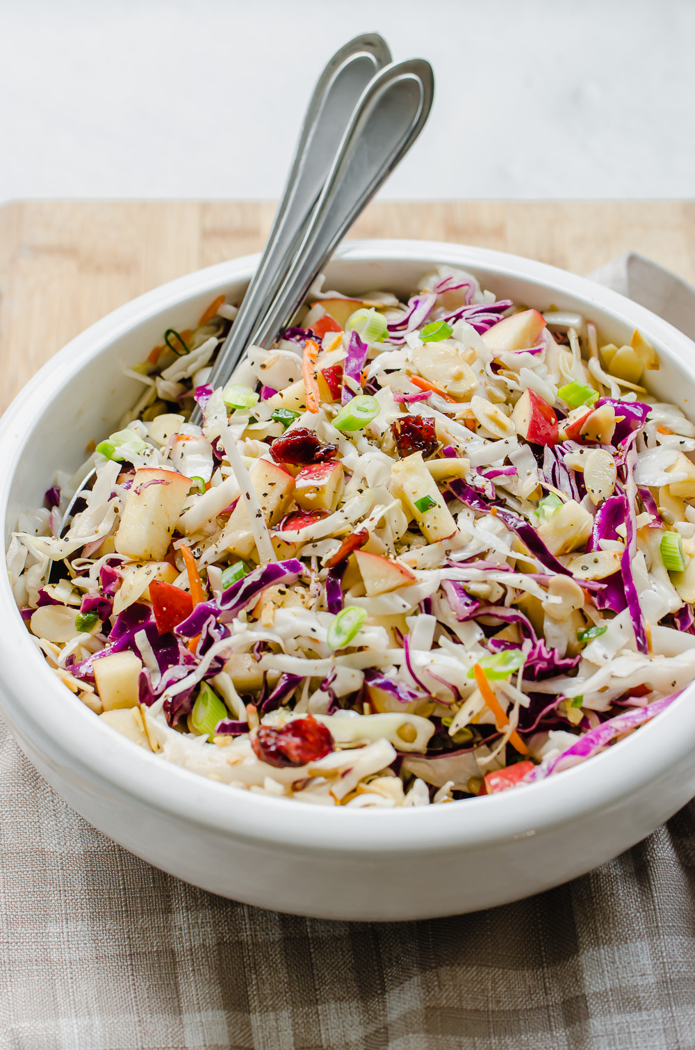 Asian slaw in a white bowl with serving spoons.
