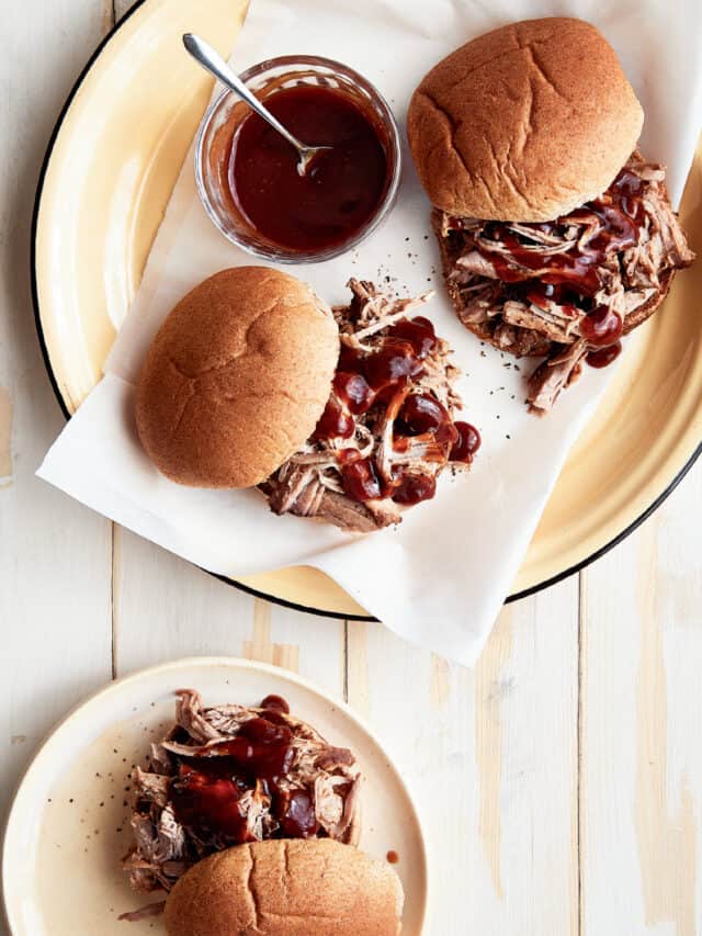 Pulled pork sandwich on a plate with a small bowl of extra BBQ sauce.