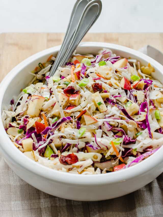 Asian slaw served in a white bowl with two spoons.