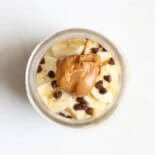 Looking into the top of a mason jar of peanut butter cup overnight oats that has banana slices, a dollop of peanut butter and mini chocolate chips on top.