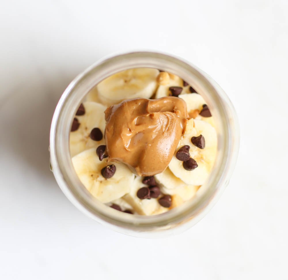 Looking into the top of a mason jar of peanut butter cup overnight oats that has banana slices, a dollop of peanut butter and mini chocolate chips on top.