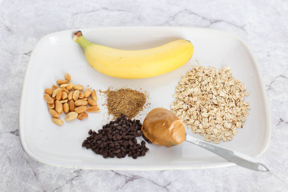 bananas, peanuts, flaxseed, mini chocolate chips, peanut butter, and rolled oats on a plate
