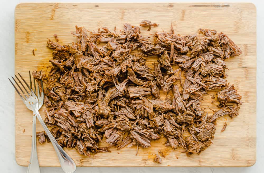 Shredded beef on a wooden cutting board with two forks.