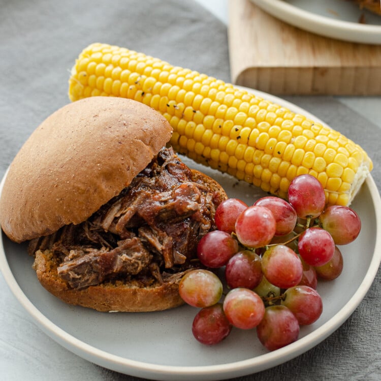 BBQ shredded beef sandwich on a plate with corn and grapes