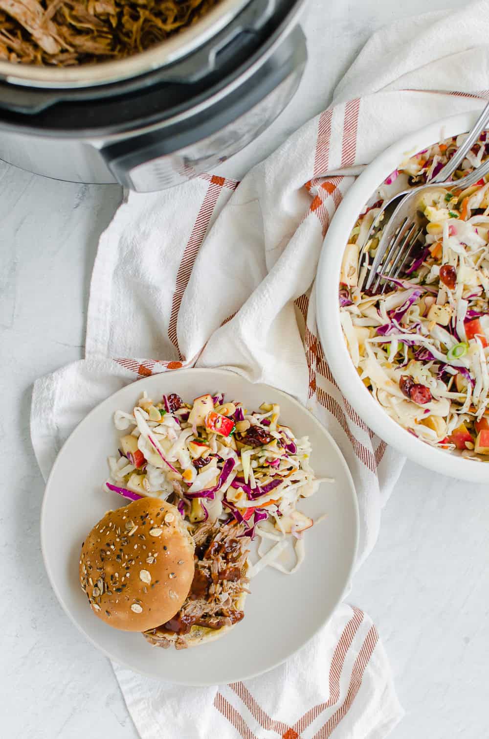 A pulled pork bbq sandwich on a white plate with slaw on the side against a white background. 