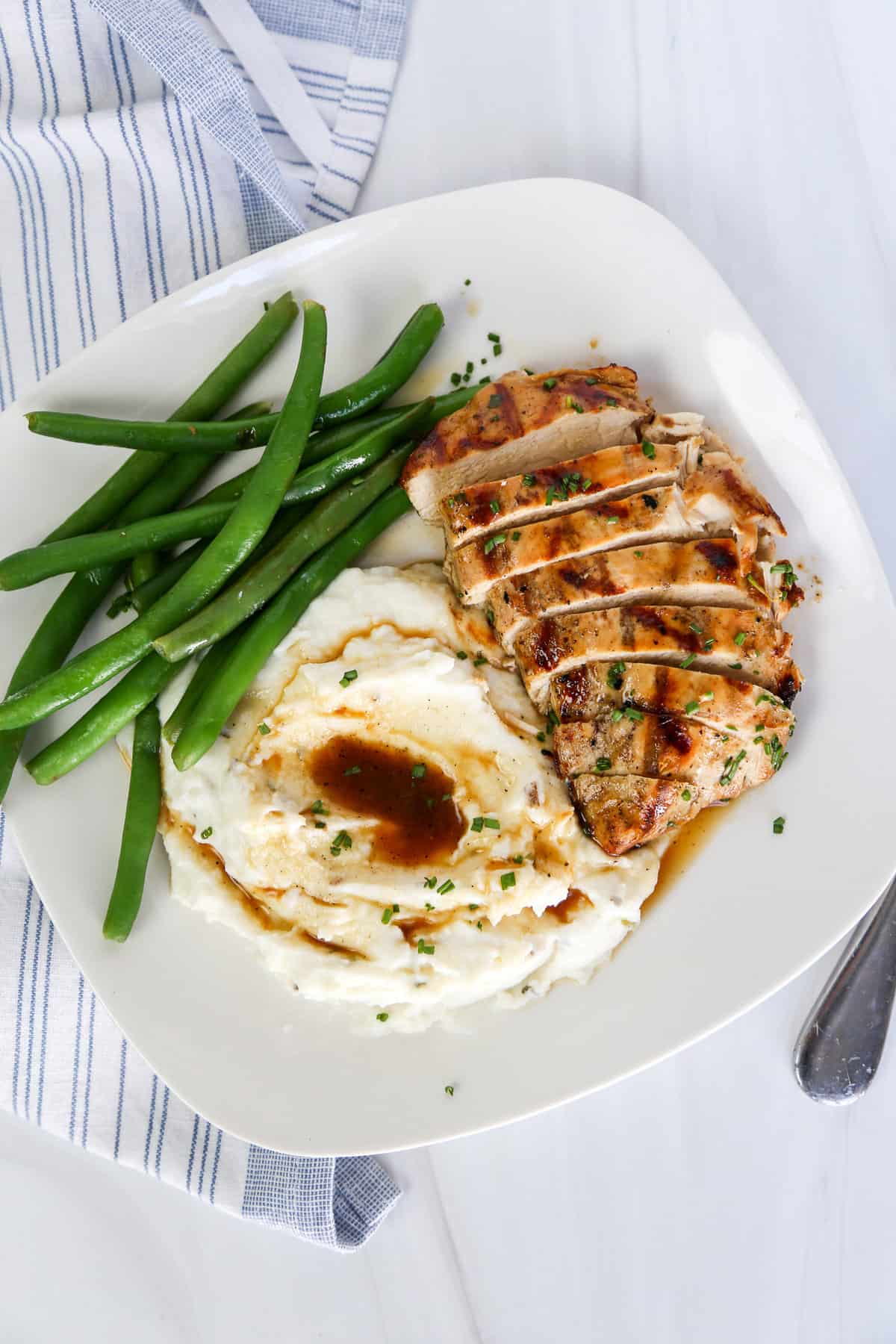 Grilled savory chicken breast with mashed potatoes and green beans on a plate.