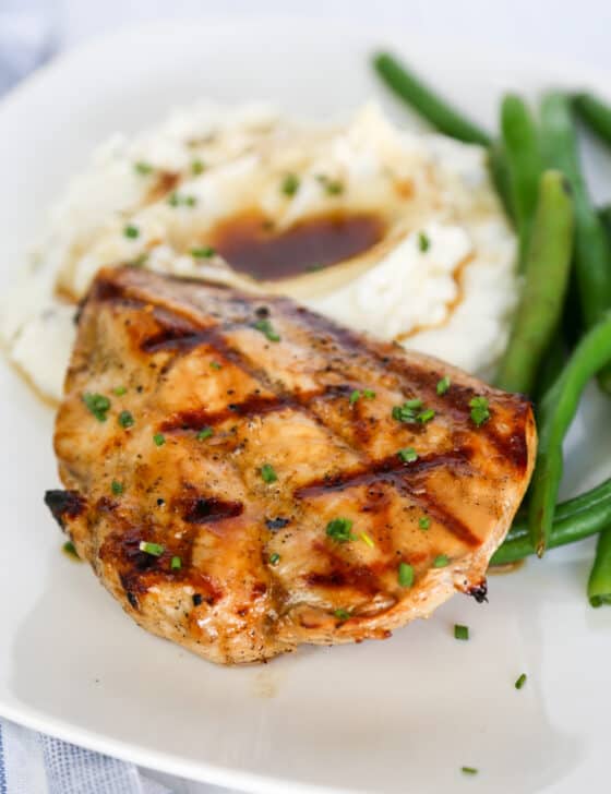 Grilled savory chicken breast with mashed potatoes and green beans on a plate.