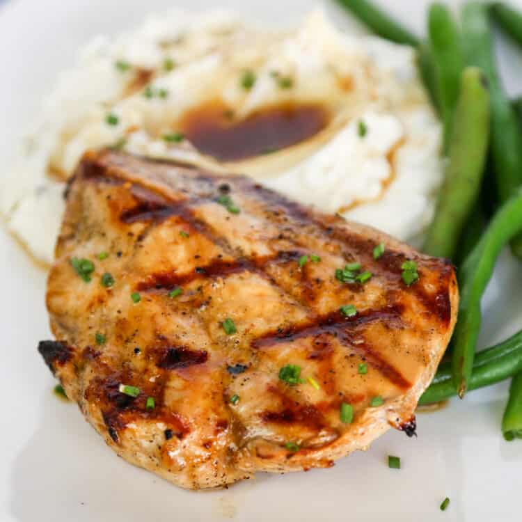 Grilled savory chicken breast with mashed potatoes and green beans on a plate.