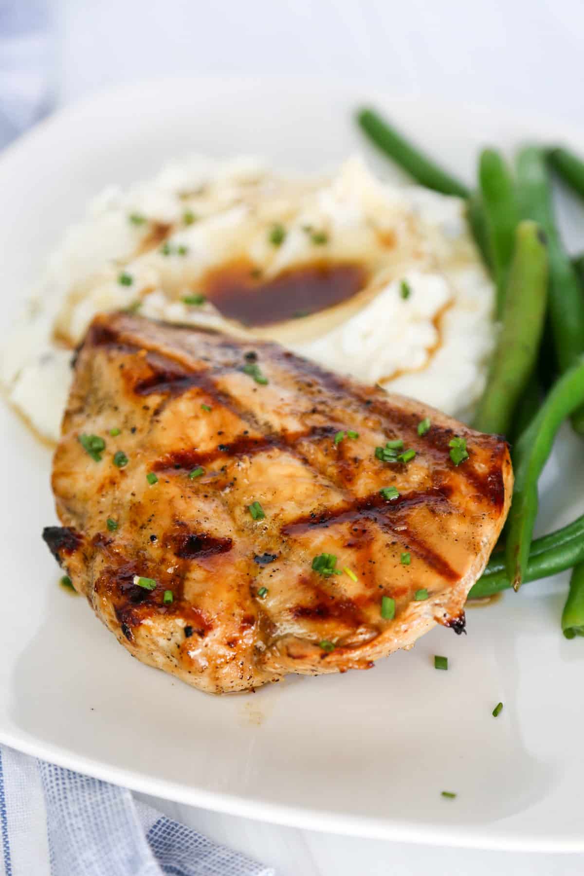 Grilled savory chicken breast with mashed potatoes and gravy and green beans on a plate.