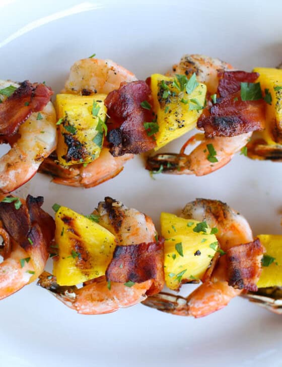Two bacon-wrapped shrimp kabobs on a white platter.