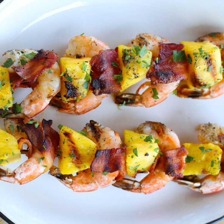 Two bacon-wrapped shrimp kabobs on a white platter.