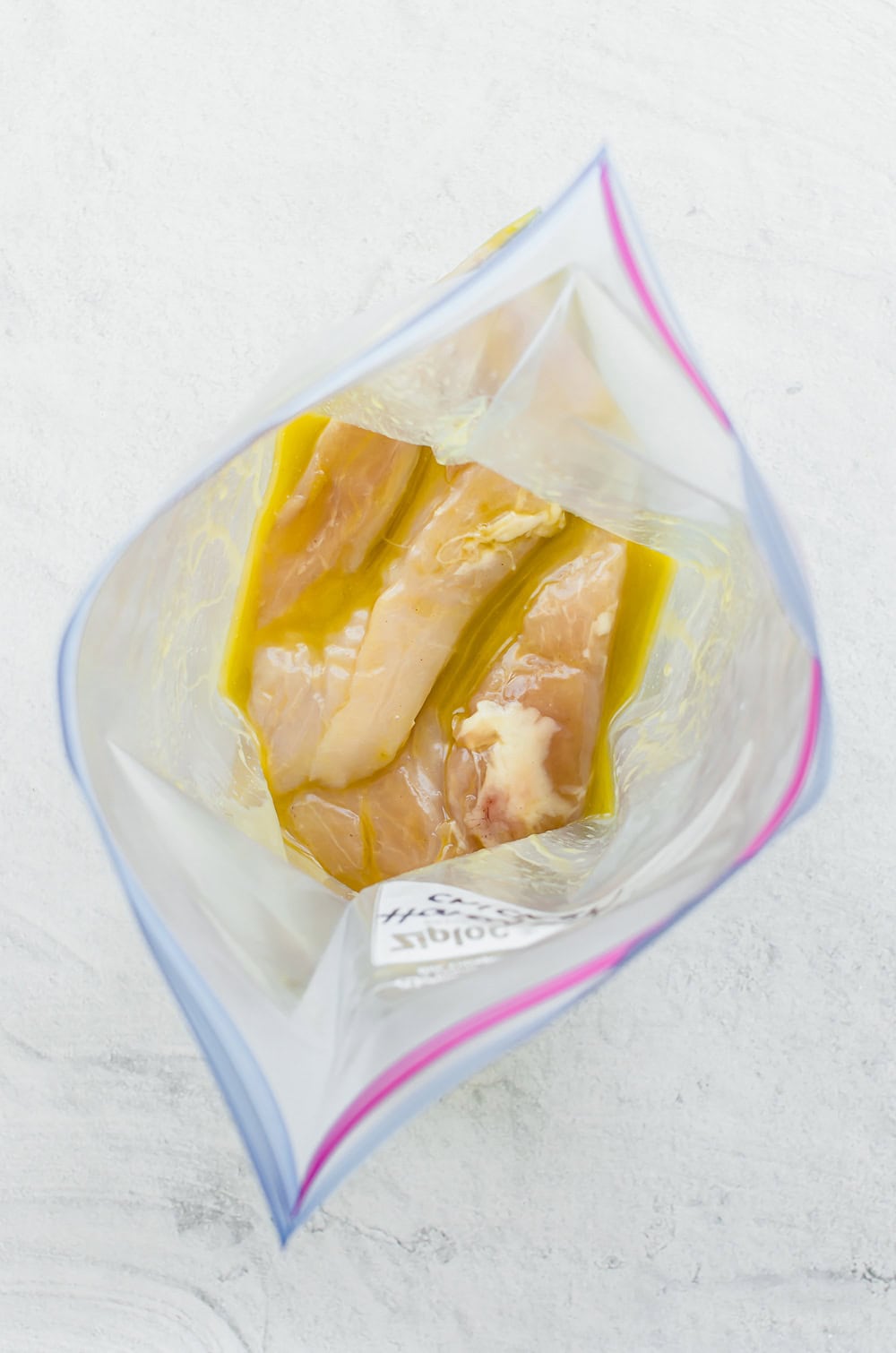 Raw chicken breasts in honey garlic marinade in a freezer bag.