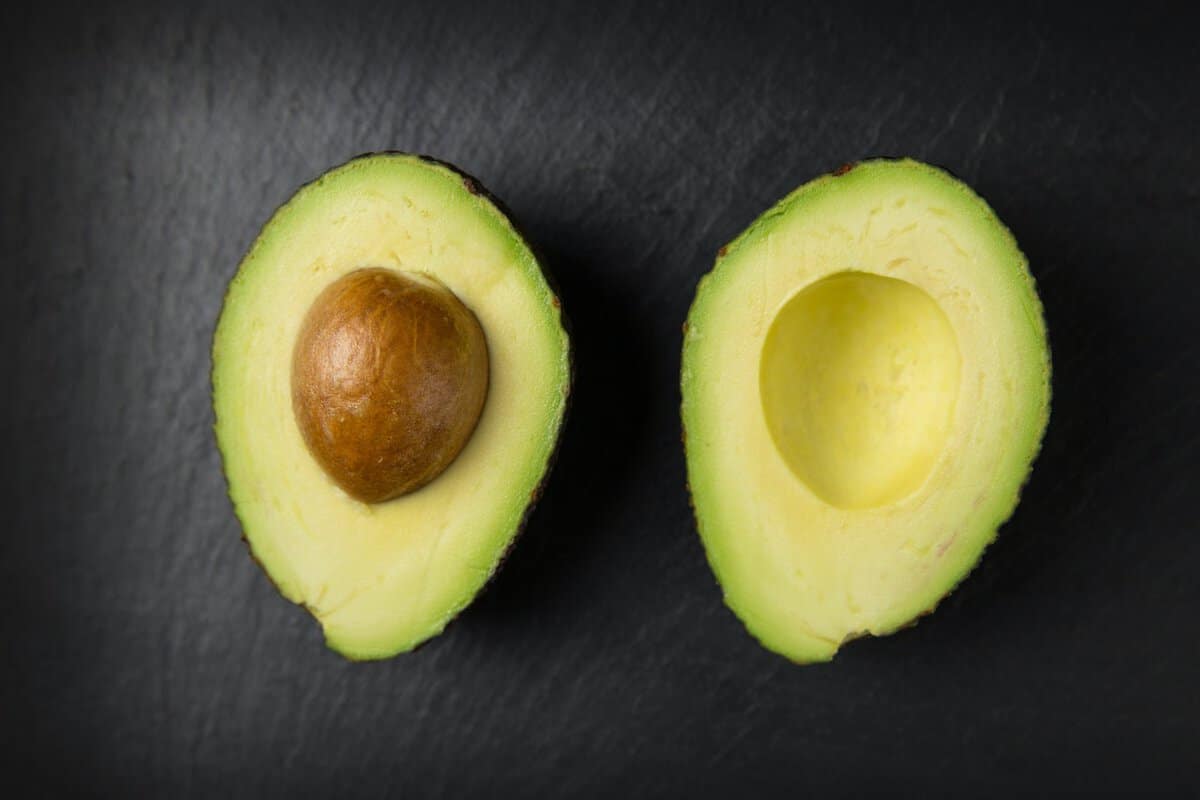 Avocado halves side by side on slate with the pit still in the left half.