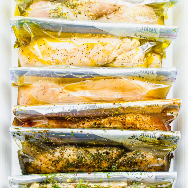7 different marinades for chicken breasts in freezer bags lined up in a container.