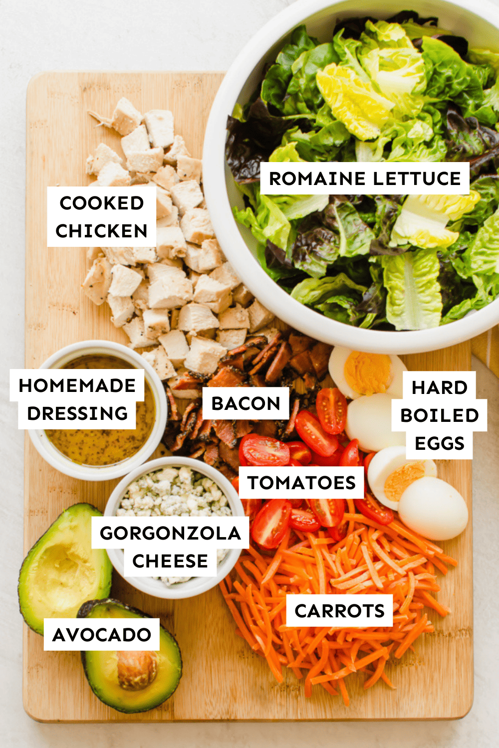 Cobb salad ingredients laid out on a wooden cutting board and labeled.
