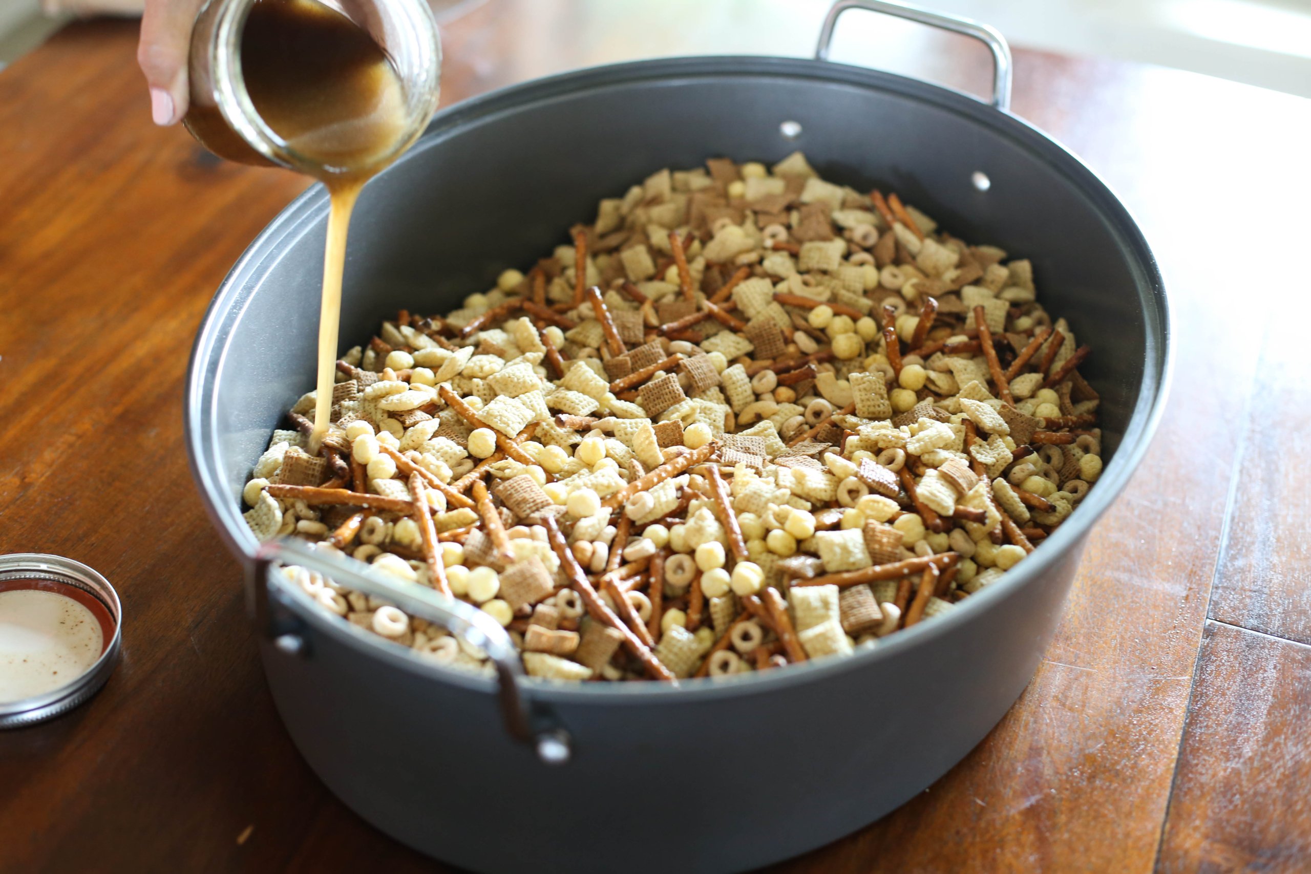 Pouring sauce over homemade chex mix in a large roasting pan.