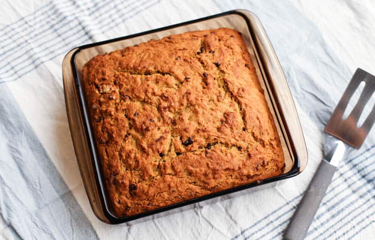 Banana breakfast cake in an 8x8 glass pan with a spatula beside it.