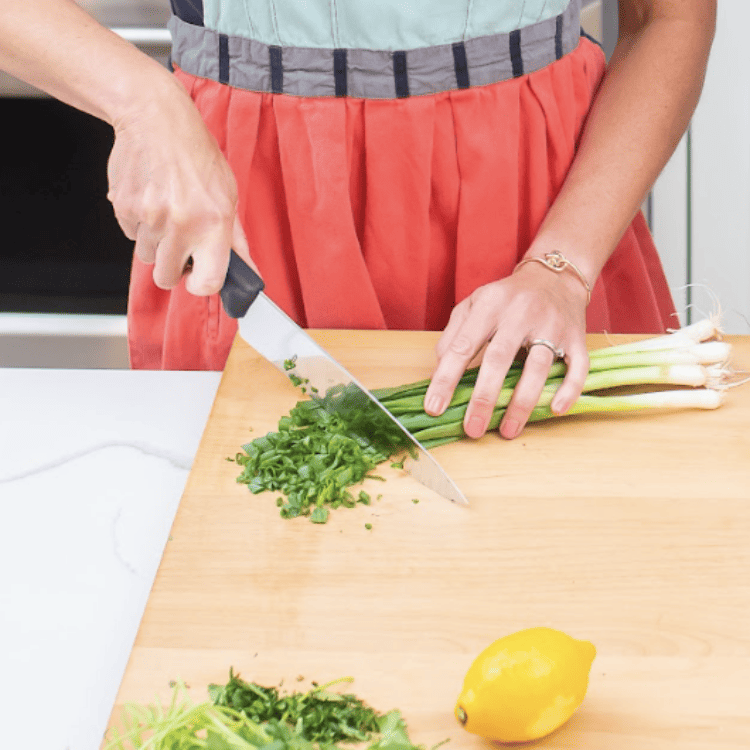 Woman chopped green onions with chef's knife.