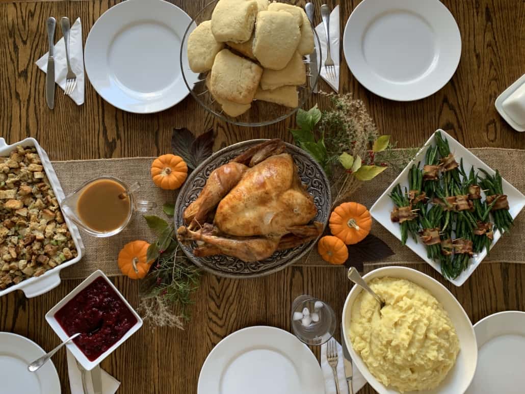 thanksgiving table setting with turkey in the center and surrounded by mashed potatoes, green beans, stuffing, and cranberry sauce