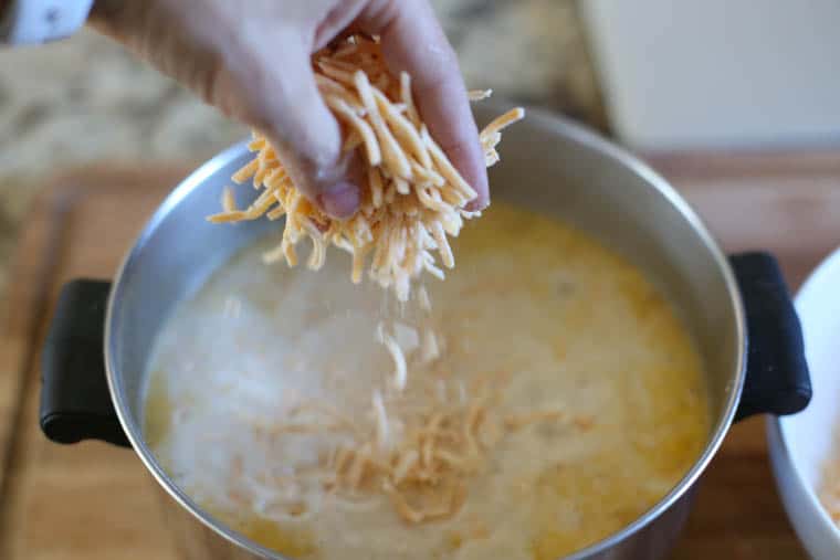 Shredded cheddar cheese being stirring into a pot