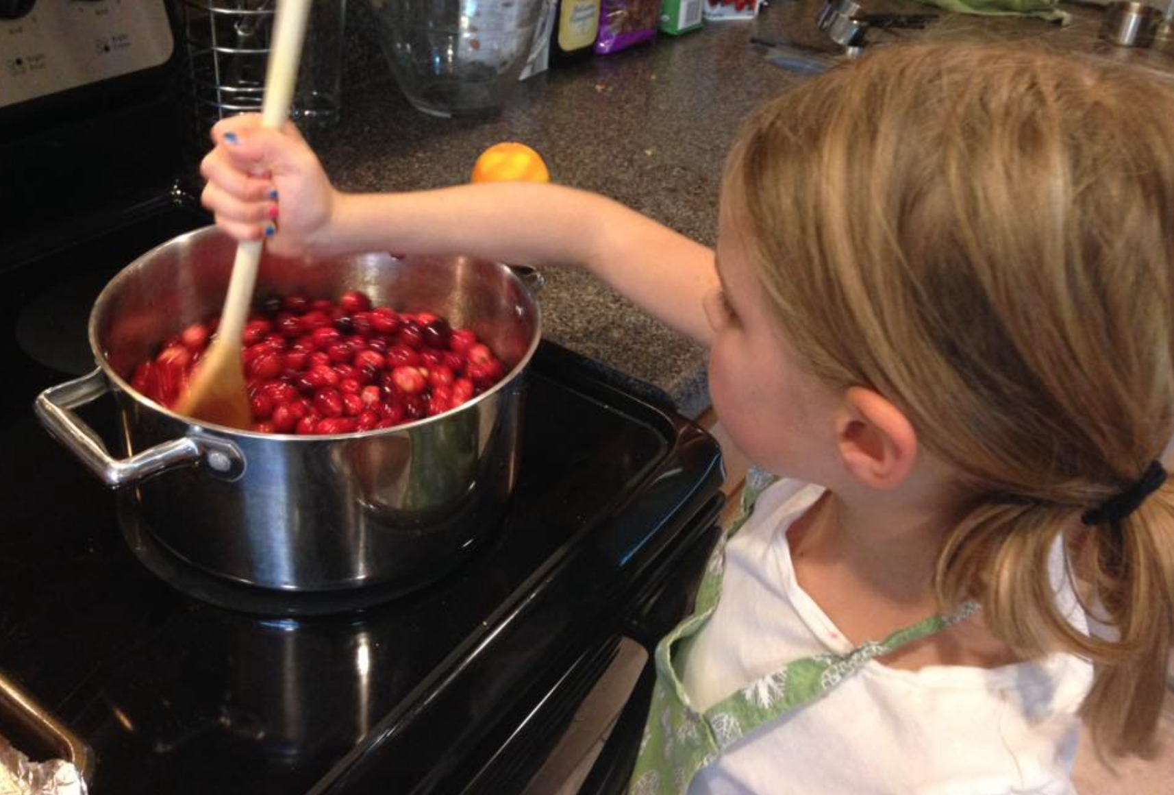 Little girl stirring homemade cranberry orange sauce in a pot on the stove.