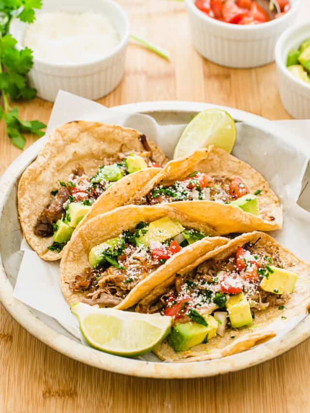 Crispy carnitas tacos in a metal dish with white bowls of toppings on the side.