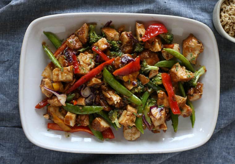 Honey bourbon chicken and vegetables on a white plate with a blue towel underneath.