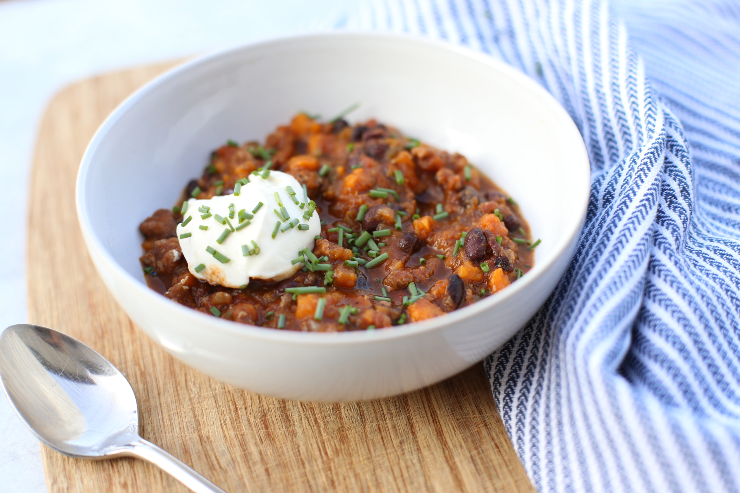 Slow cooker turkey chili with sweet potato and black beans served in a white bowl with a dollop of sour cream.