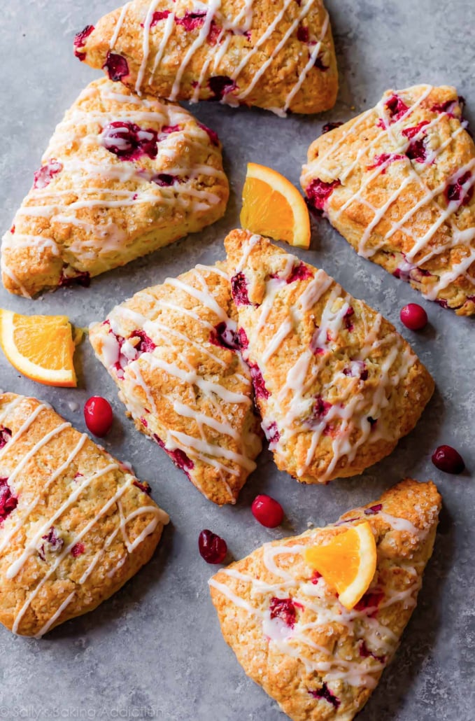 A festive Christmas breakfast idea: glazed cranberry orange scones on a gray surface with orange slices around