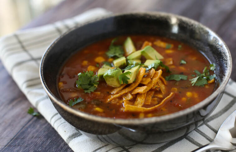 Bowl of vegetarian tortilla soup with avocado and cilantro on top.