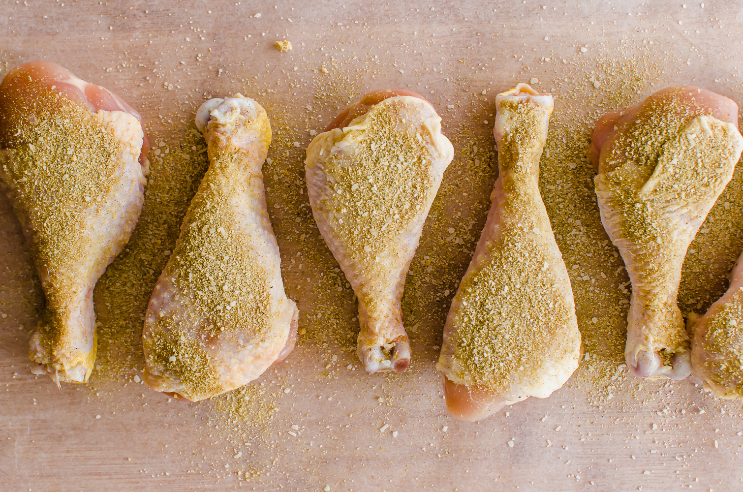 Seasoned chicken drumsticks lined up on a cutting board.