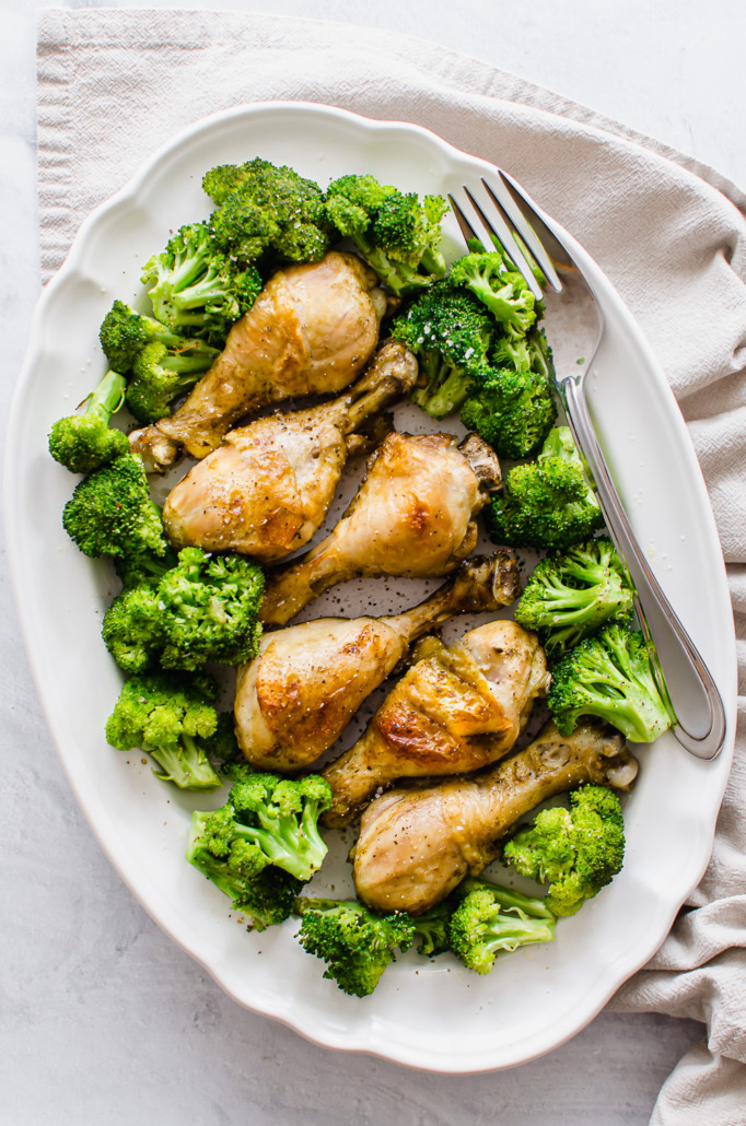 cooked chicken drumsticks on a serving platter with broccoli
