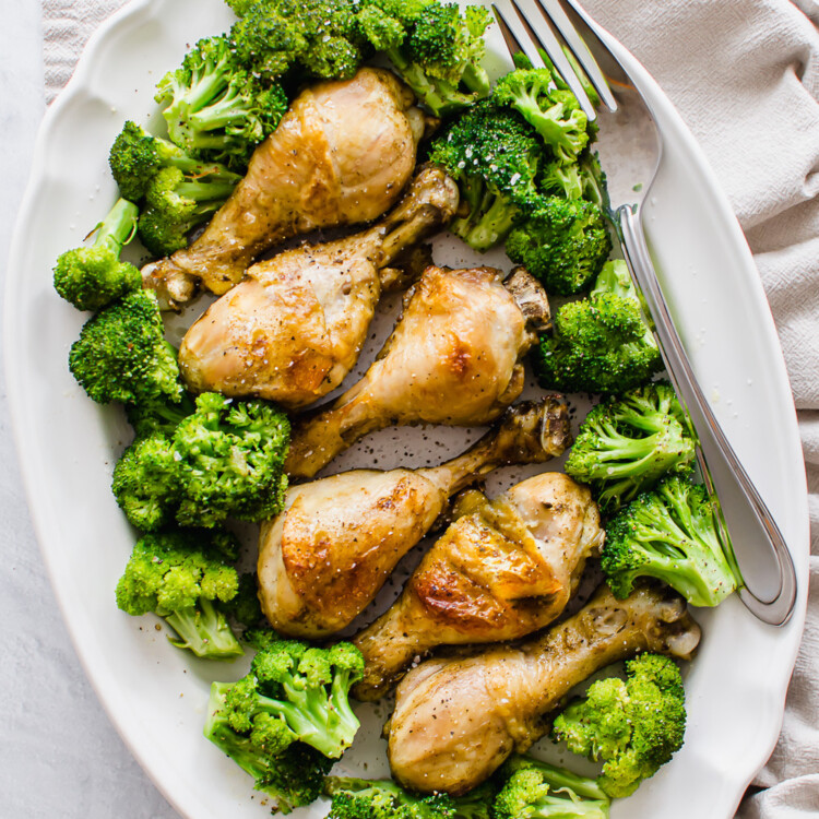 Cooked chicken drumsticks on a serving platter with steamed broccoli.