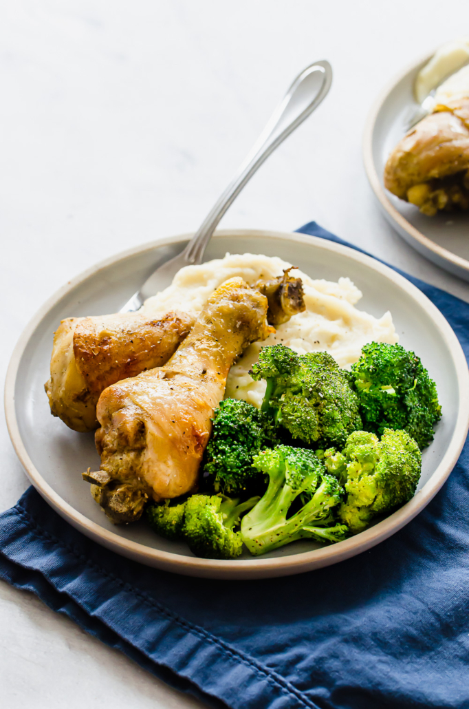 cooked chicken drumsticks on a plate with broccoli and mashed potatoes