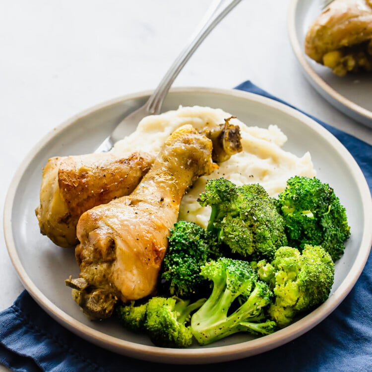 cooked chicken drumsticks on a plate with broccoli and mashed potatoes