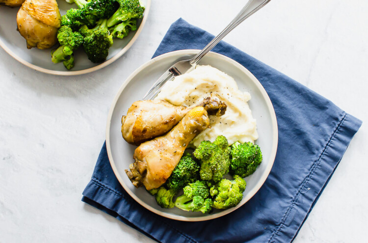 Baked chicken drumsticks on a plate with broccoli and mashed potatoes.