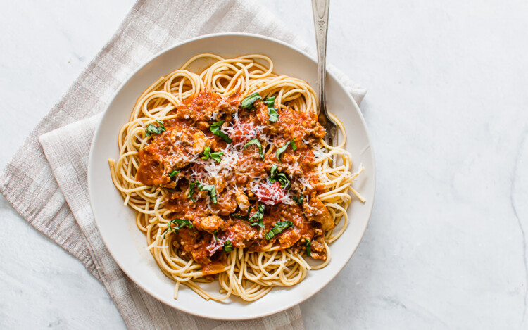 Whole wheat spaghetti with meat sauce served on a plate with fresh parsley on top.