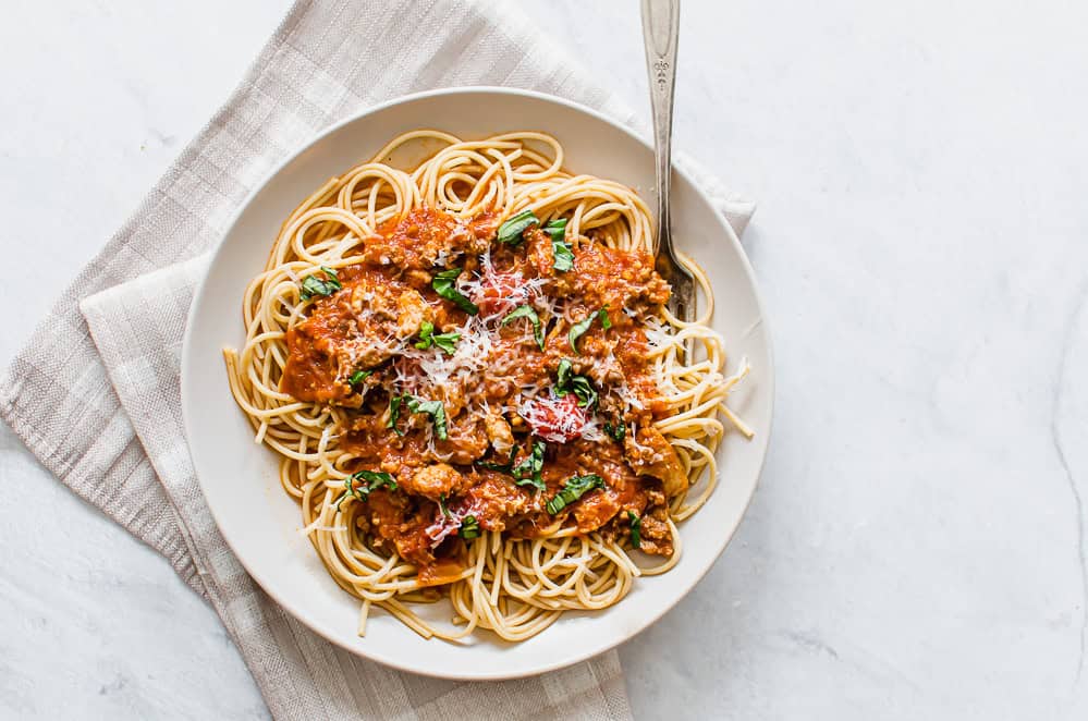 Whole wheat spaghetti with meat sauce served on a plate with fresh parsley on top.