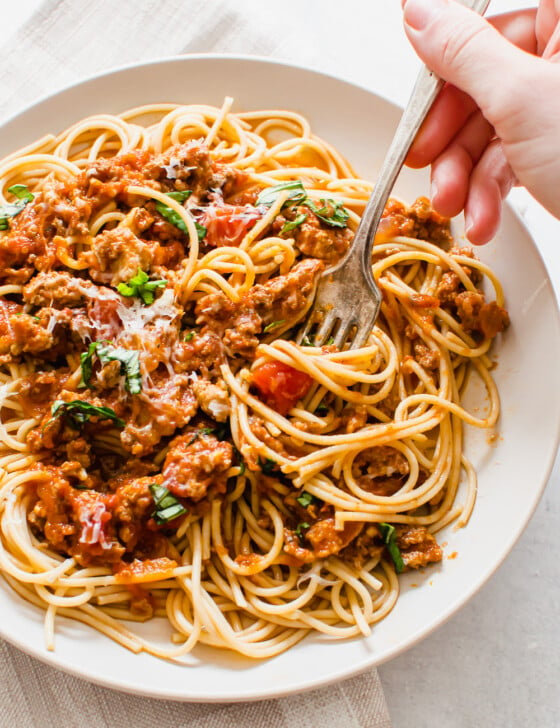 a hand with a fork twirling a bite of spaghetti on a plate