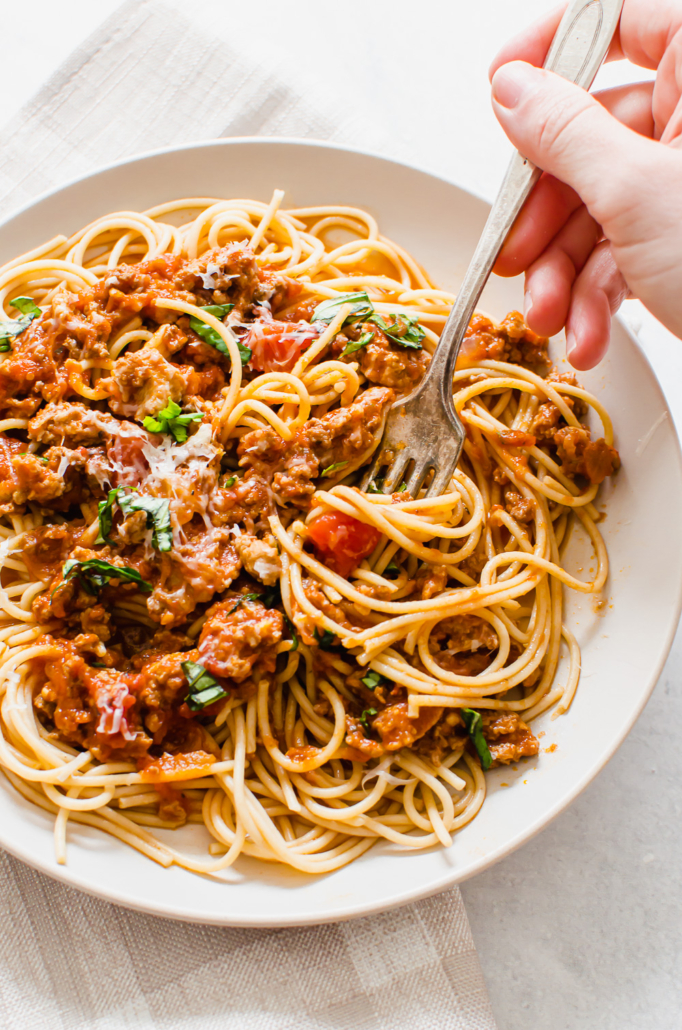 a hand with a fork twirling a bite of spaghetti and meat sauce on a plate