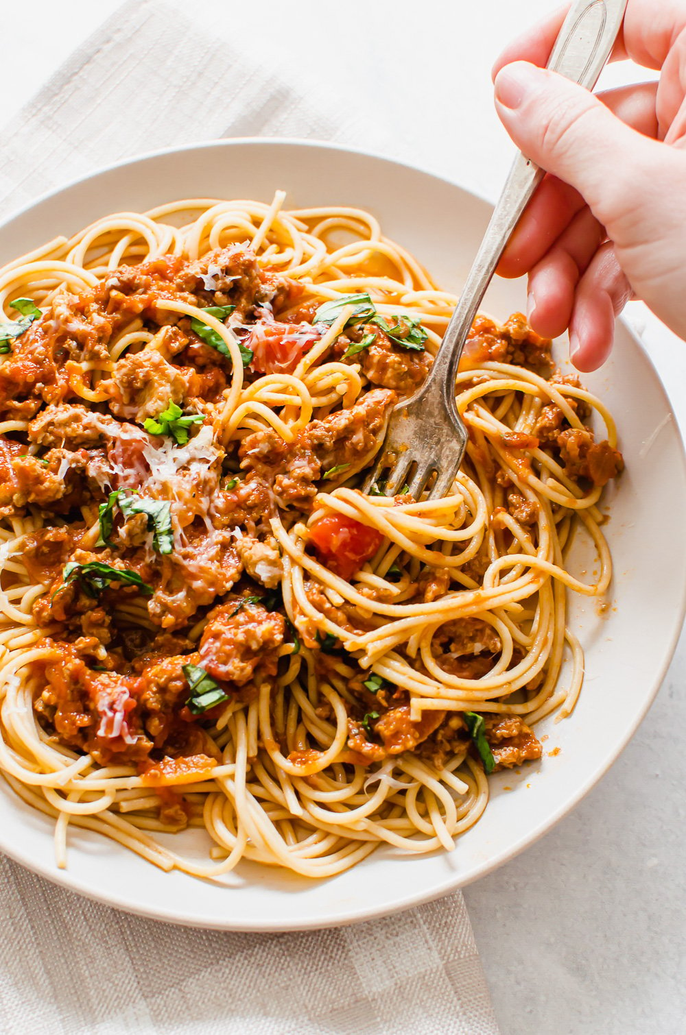 A hand with a fork twirling a bite of spaghetti and meat sauce on a plate.