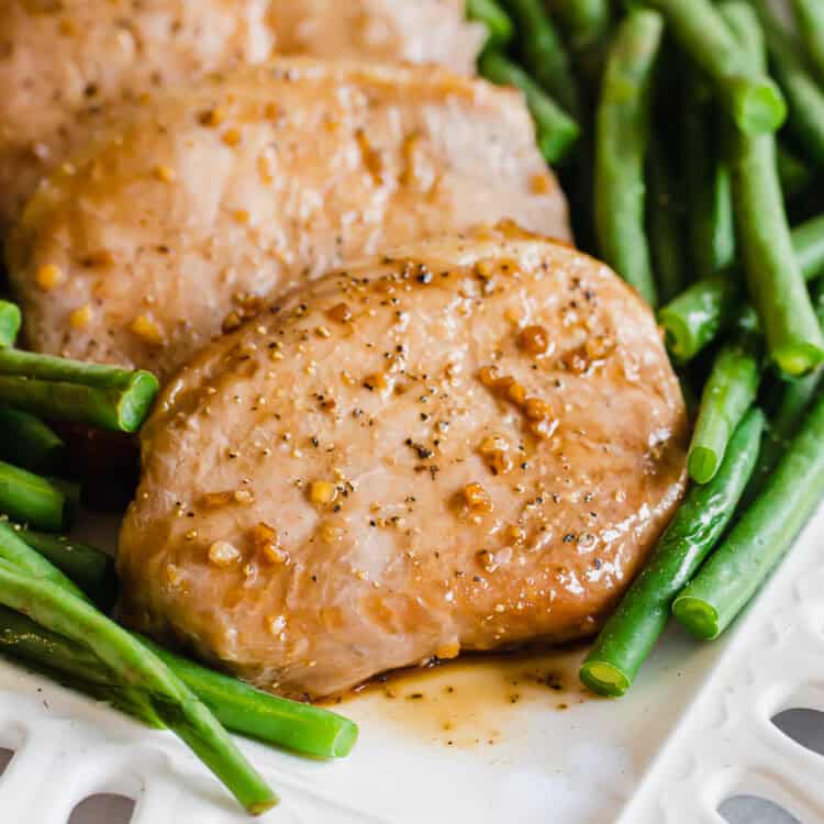 Four savory pork chops lined up on a plate wit green beans on either side of them.