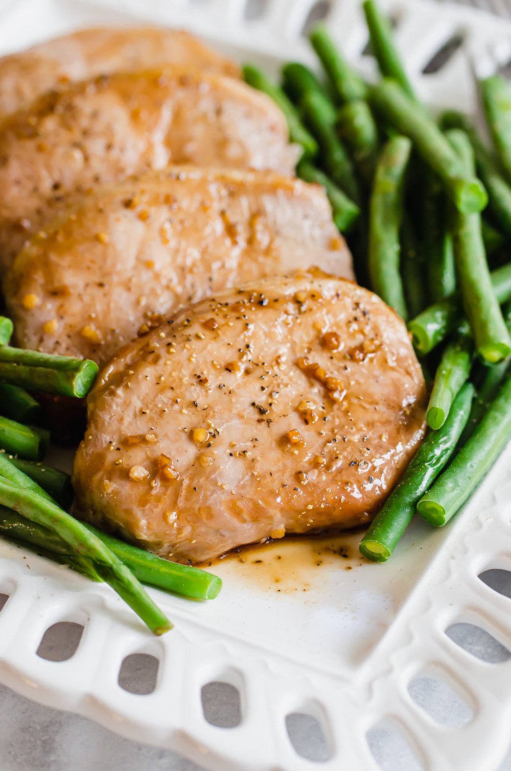 Four savory pork chops lined up on a plate with green beans on either side of them.