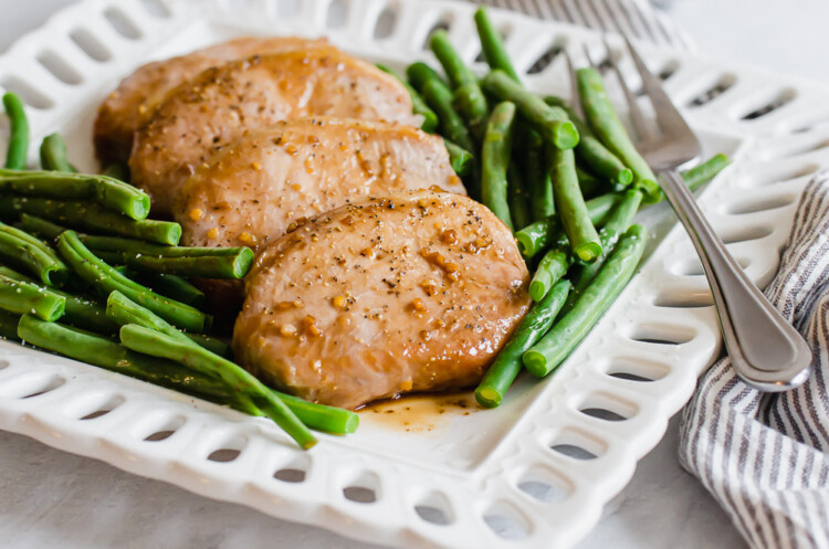 Sweet and savory pork chops on a white platter with green beans surrounding the chops.