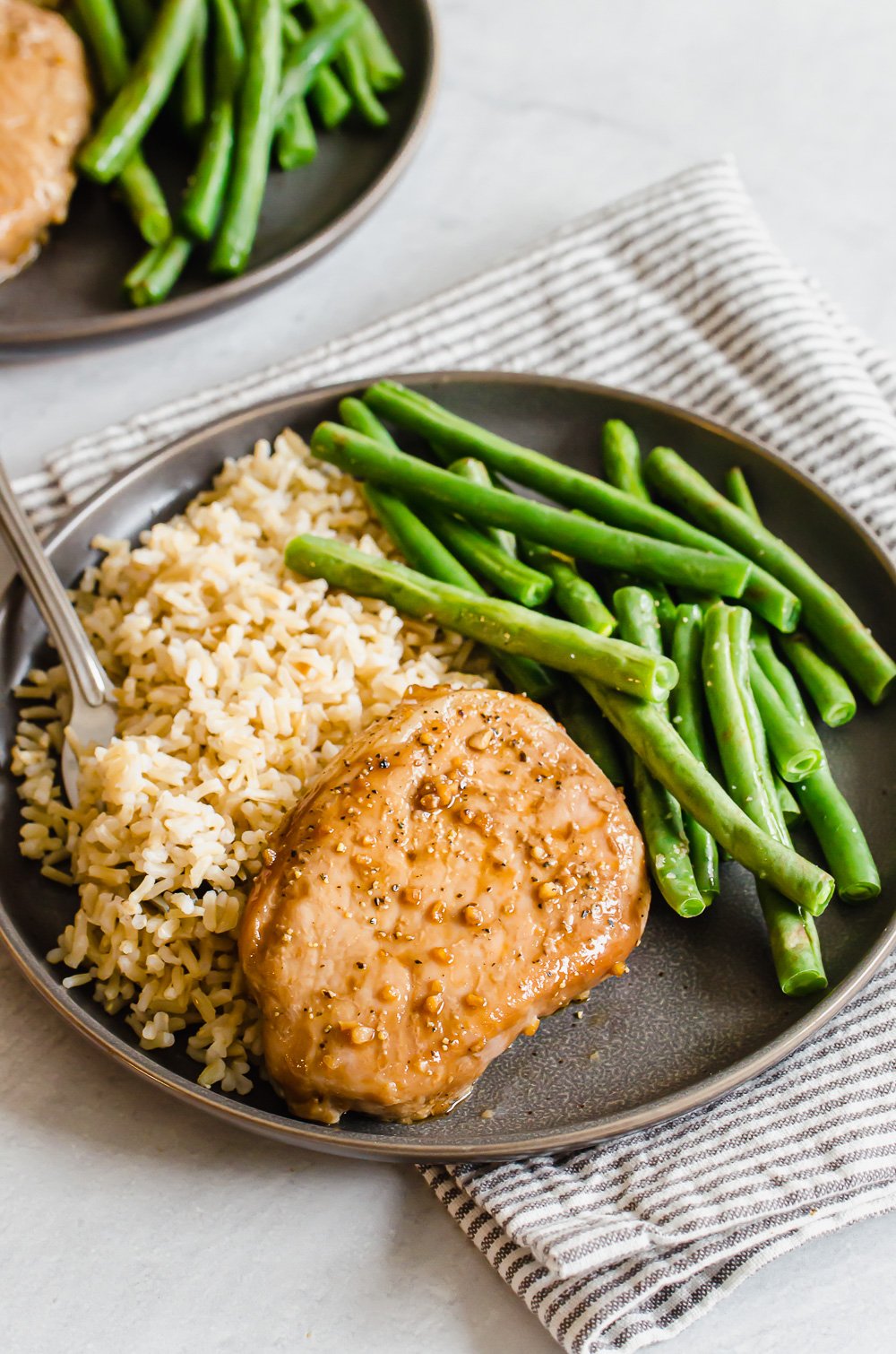 Sweet and savory baked pork chop on a plate with rice and green beans on the side.