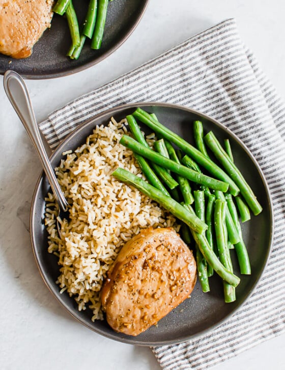 Savory baked pork chop on a gray plate with rice and green beans.