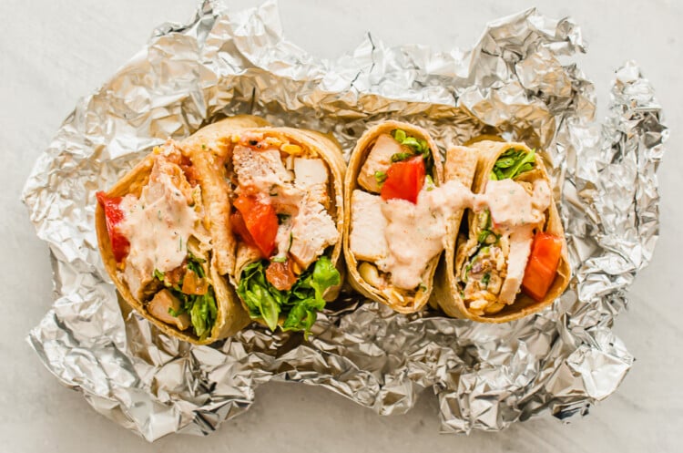 Two Southwest chicken wraps cut in half with foil around them.