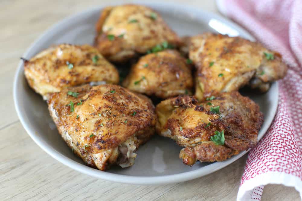 Italian baked chicken thighs on a white plate with a red and white towel on the side. 