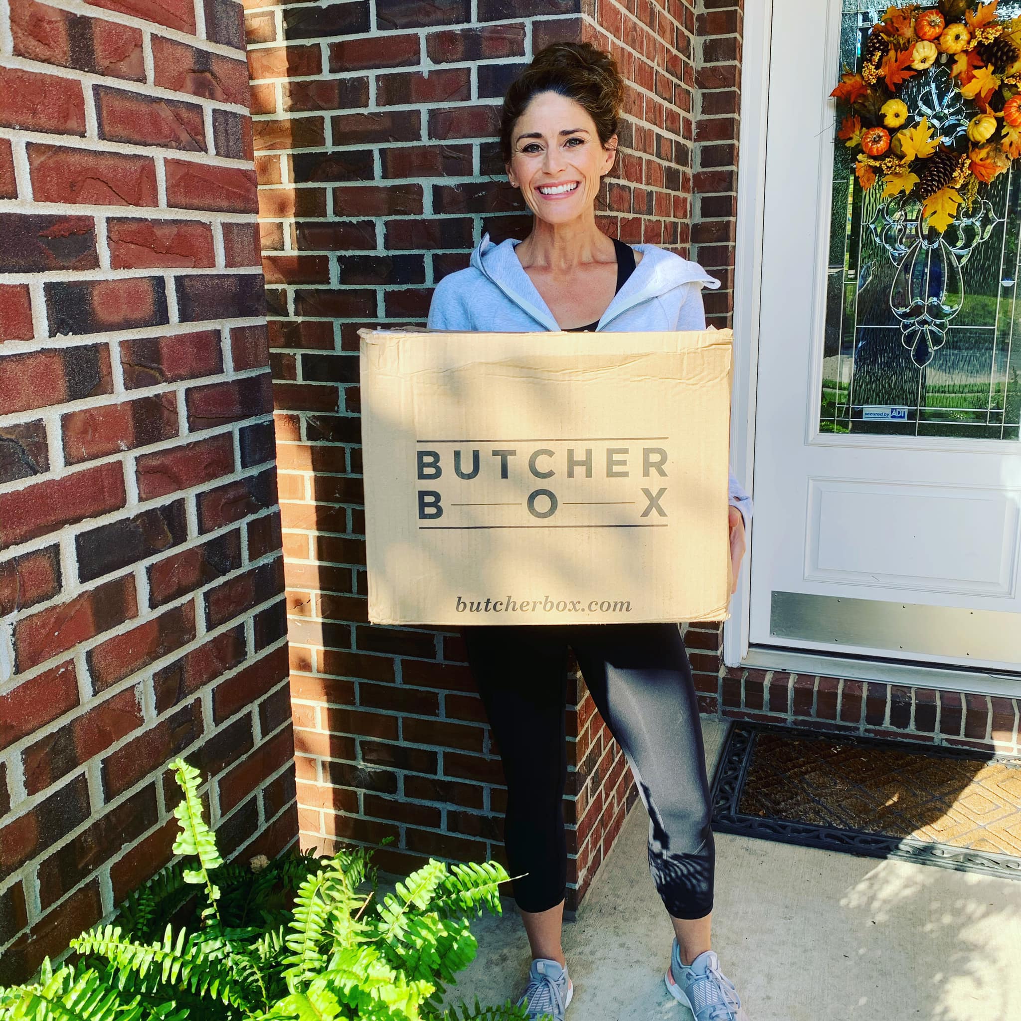 Woman holding a ButcherBox box on her front porch.