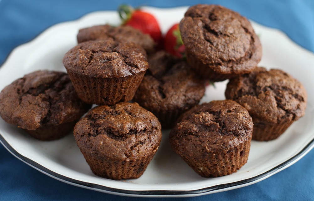 Chocolate banana muffins stacked up on a plate with strawberries in the background.
